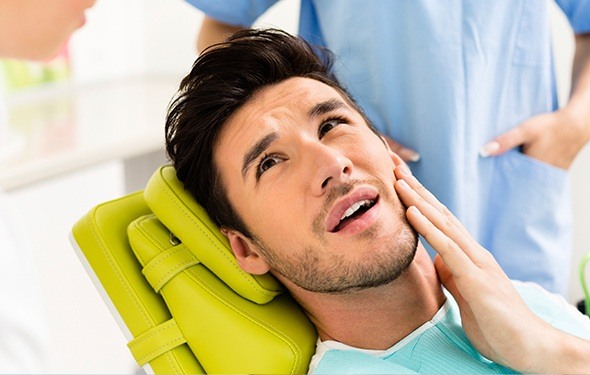 Man in dental chair holding jaw